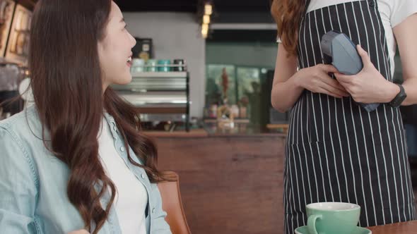 Asian freelance women pay contactless credit card at coffee shop. Asian happy girl barista.