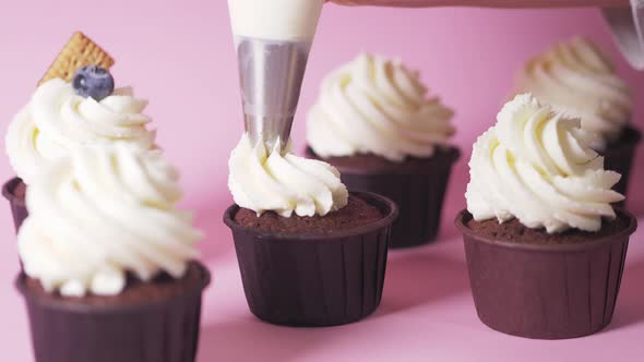 Applying White Cream on a Dark Chocolate Cupcake Cupcake on a Pink Background