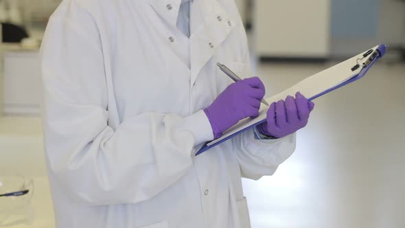 Portrait of Female writing down notes on notepad in science laboratory and looking to camera