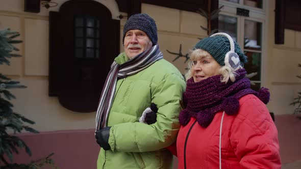 Front View of Senior Couple Tourists Man Woman Walking Talking Gesturing in Winter Holiday City