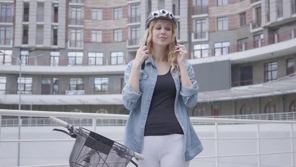 Pretty Blond Woman Putting a Bike Helmet on Her Head and Riding Her Bicycle Against the Background