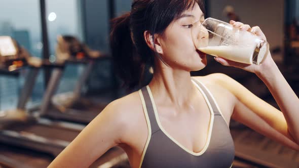 Attractive fitness asian woman finishing workout and drinking protein milk shake vitamins