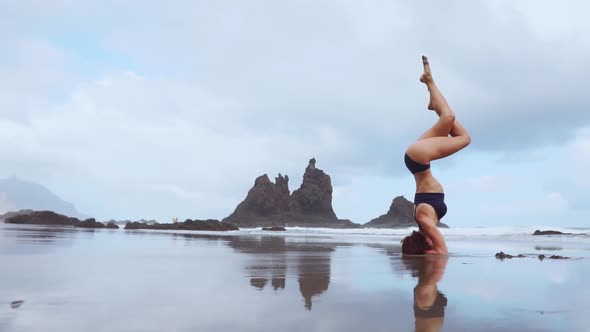 Sports Girl Standing on Her Head on the Ocean Moves Her Legs in the Air