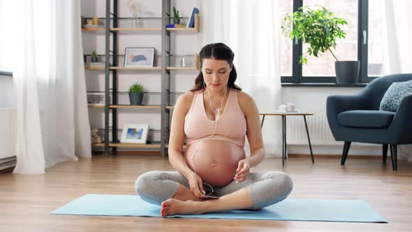 Pregnant Woman with Earphones Doing Yoga at Home