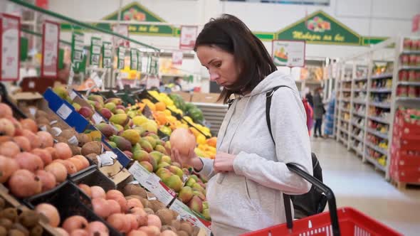 Midrange Caucasian Woman in a White Sweater in a Shopping Mall with Fruits in a Supermarket Buys a