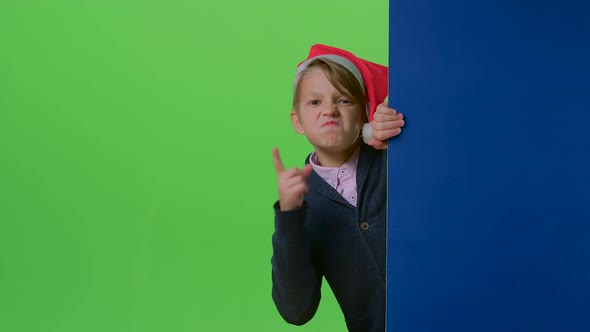 Teenage Boy in Christmas Hat Emerges From Behind the Boards and Waving His Index Finger on a Green