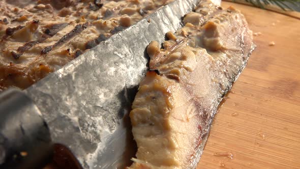 Super Closeup of a Knife Taking a Piece of Mackerel Fish From the Wooden Board