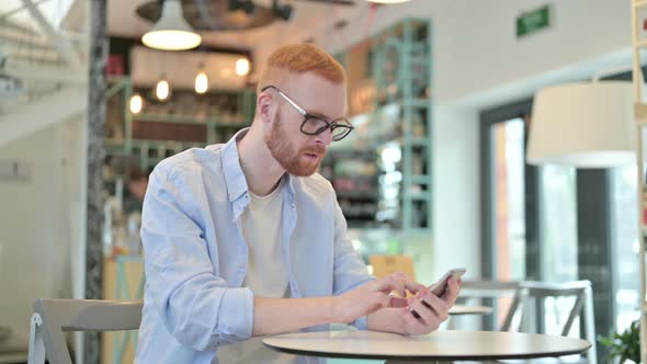 Redhead Man Celebrating Success on Phone in Cafe 