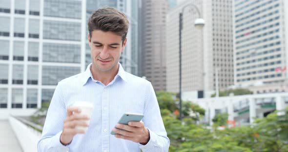 Businessman using mobile phone and holding cup of coffee