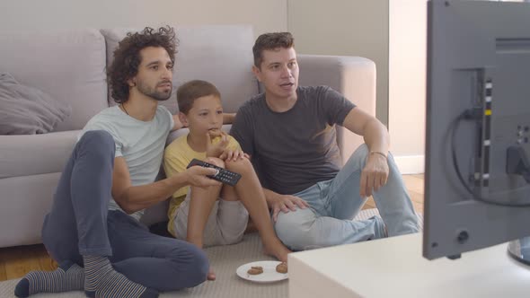 Focused Boy and His Fathers Eating Cookies and Watching Movie