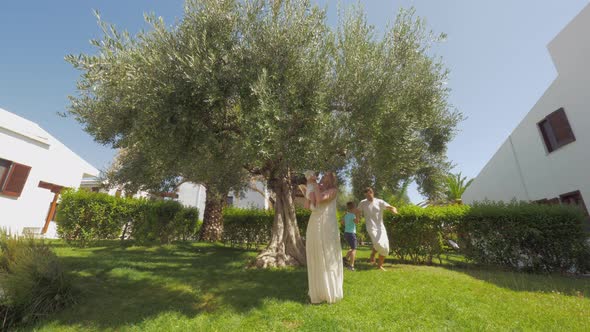 Happy parents and children in green garden with big olive tree