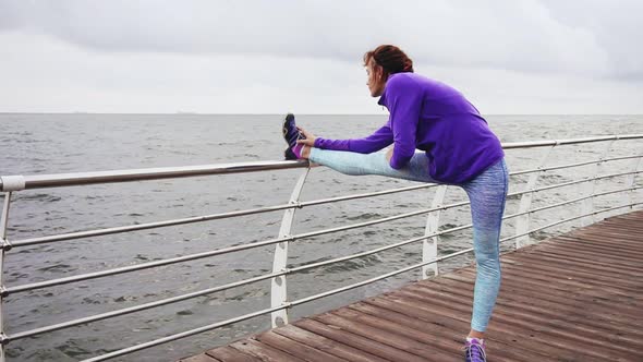 Athletic Woman Stretching Her Legs Before a Jog on the Beach By the Sea Early in the Morning