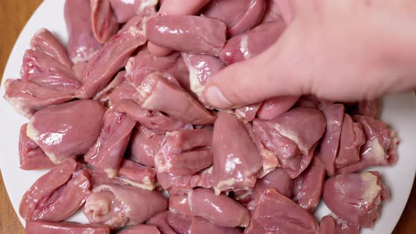 Female Hand Puts Fresh Raw Peeled Chicken Hearts on a Plate