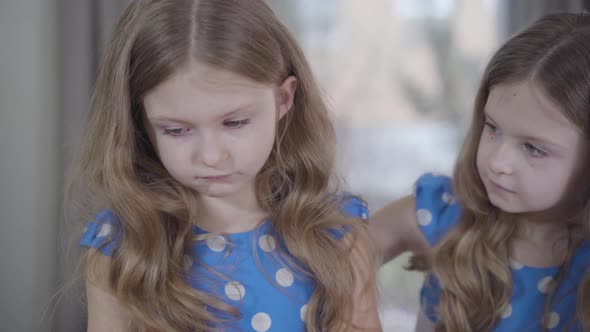 Close-up Portrait of Upset Caucasian Little Girl Yelling at Twin Sister and Turning Back To Camera