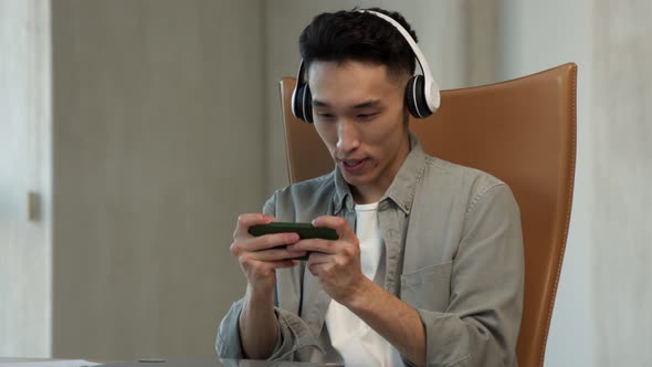 Asian Man Plays Racing Game in Smartphone at Workplace