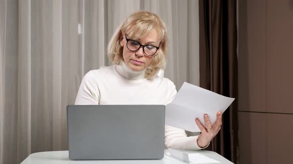 Woman of Middle Age in Glasses Counts Utility Bills at Table