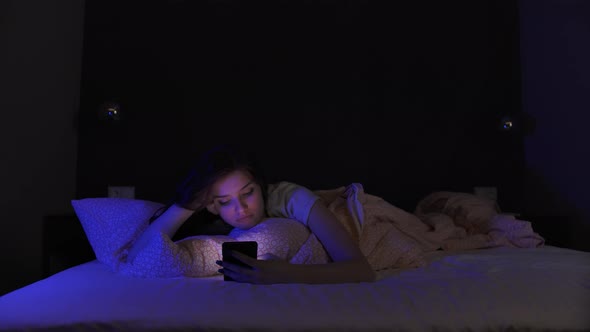 Teenage Girls Lying On Bed Using Smartphone Texting On Social Media Browsing Online At Weekend 