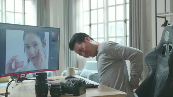 Asian Cameraman Having Backache While Using Desktop Computer For Working At Home