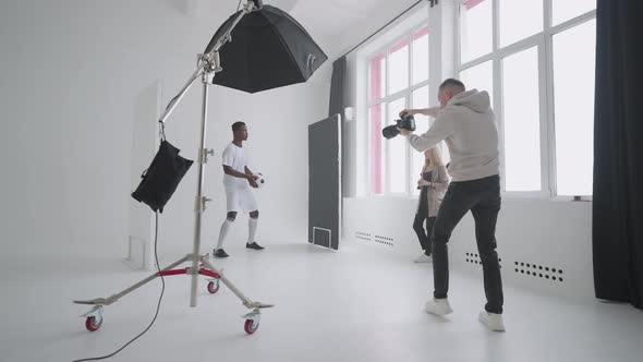 Afroamerican Footballer is Playing with Ball and Posing for Photographer During Shooting for