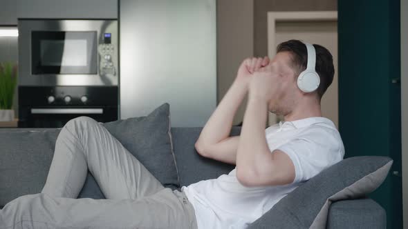 Young Man Enjoying Listening to Music with Headphones While Lying on the Sofa at Home