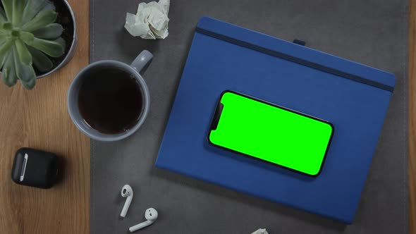 A Mobile Phone with a Green Screen Lies on a Notepad on the Desktop Closeup