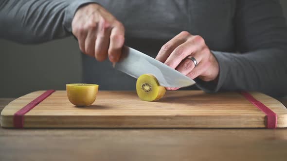 close up shot of man slicing kiwi. Wooden chopping board and chef casually dressed