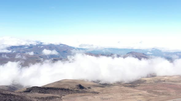 Aerial view showing a barren landscape with white clouds flowing over the landscape