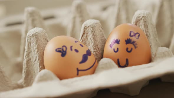 Video of close up of two brown eggs with drawn faces in egg carton background