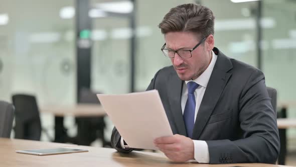 Serious Middle Aged Businessman Doing Paperwork in Office