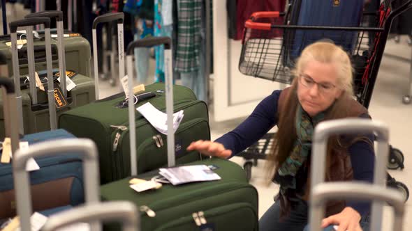 Blonde woman looking for carry on luggage in a hypermarket.