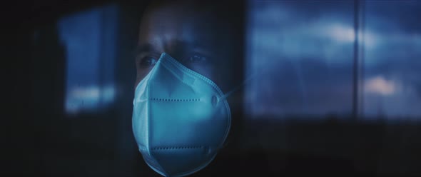 Man putting his hands on a window while wearing a medical mask