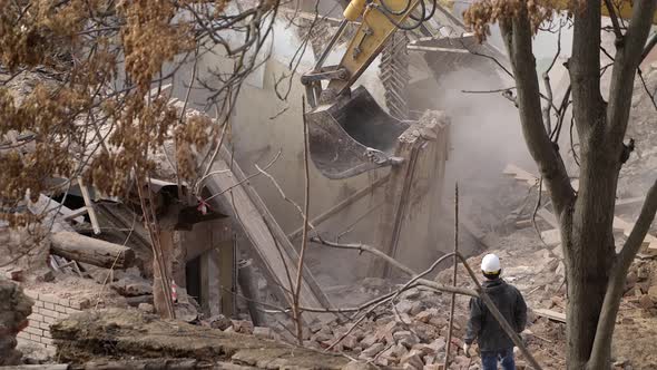 Engineer with Protective Helmet Looks at Demolition Destruction of Old Building Excavator Breaks