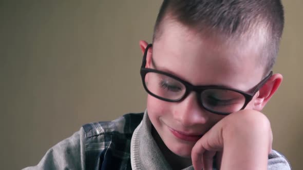 Close-up face of a caucasian boy wearing glasses 5-7 years old diligently doing homework, a child we