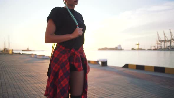 Young Stylish Funky Girl with Green Hair Riding Roller Skates and Dancing Near Sea Port During