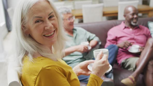 Animation of happy diverse female and male senior friends drinking coffee at home