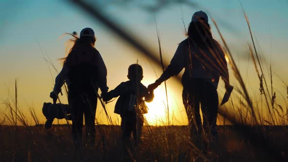 Silhouettes of Mother with Two Kids Hiking on Nature on Sunset. Concept of Friendly Family.