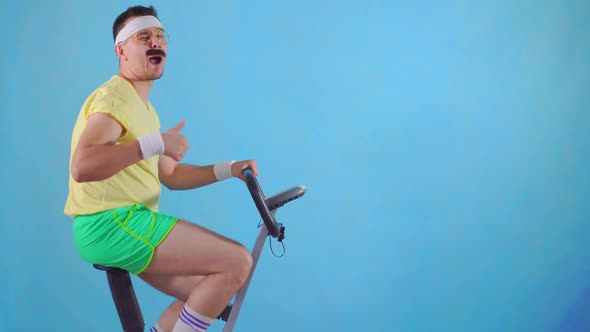 Funny Man From the 80's with a Mustache on Exercise Bike on a Blue Background Shows Thumb Up