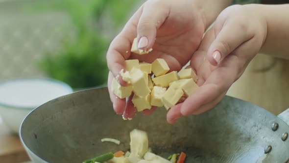 Woman adding cheese cubes in frying pan