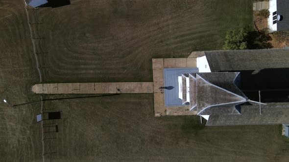 Still top-down aerial view of a tiny person coming out of church and walking along narrow paved path