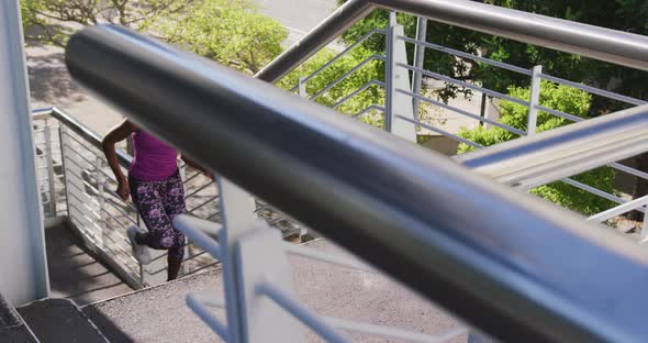 African american woman wearing earphones climbing up the stairs of the city bridge
