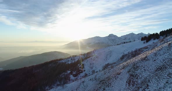 Forward Aerial Top View Over Winter Snowy Mountain and Woods Forest at Sunset or Sunrise