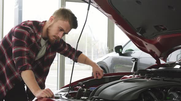 Handsome Male Cutomer Examining Engine of a Car at the Dealership Showroom