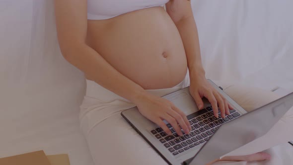 Pregnant business woman sitting and working on the laptop with sale report,tablet,books at home