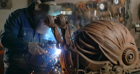 Locksmith Welds the Decorative Metal Steampunk Snail Sculpture with a Lot of Sparks and Flashes in