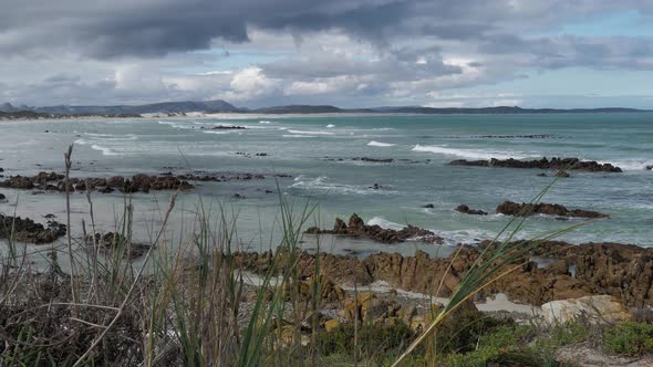 Waves running out onto rocky beach with dramatic stormy skies, panning shot