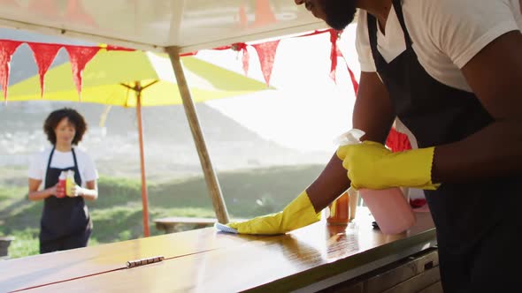 African american man wearing apron and gloves cleaning the food truck with disinfectant spray