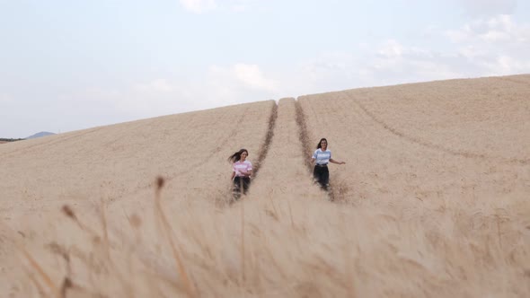 Two young female friends enjoying the nature together while walking in a wheat field.