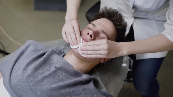 Beautician's Hands Wipe the Man's Face with Cotton Swabs During the Procedure