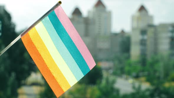 Flag of the LGBTQ set against blue sky and city street. Rainbow stripes on colorful LGBT flag