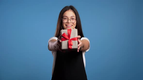 Pretty Brunette Asian Girl in Glasses Gives Gift and Hands It To the Camera. She Is Happy